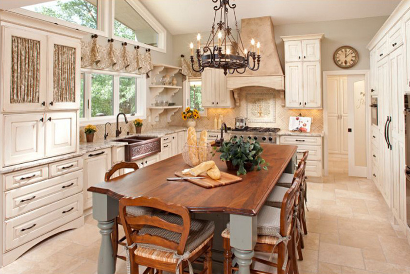 Large farmhouse l-shaped travertine floor and brown floor kitchen photo in New York with a farmhouse sink, raised-panel cabinets, white cabinets, granite countertops, brown backsplash, ceramic backsplash, stainless steel appliances and an island