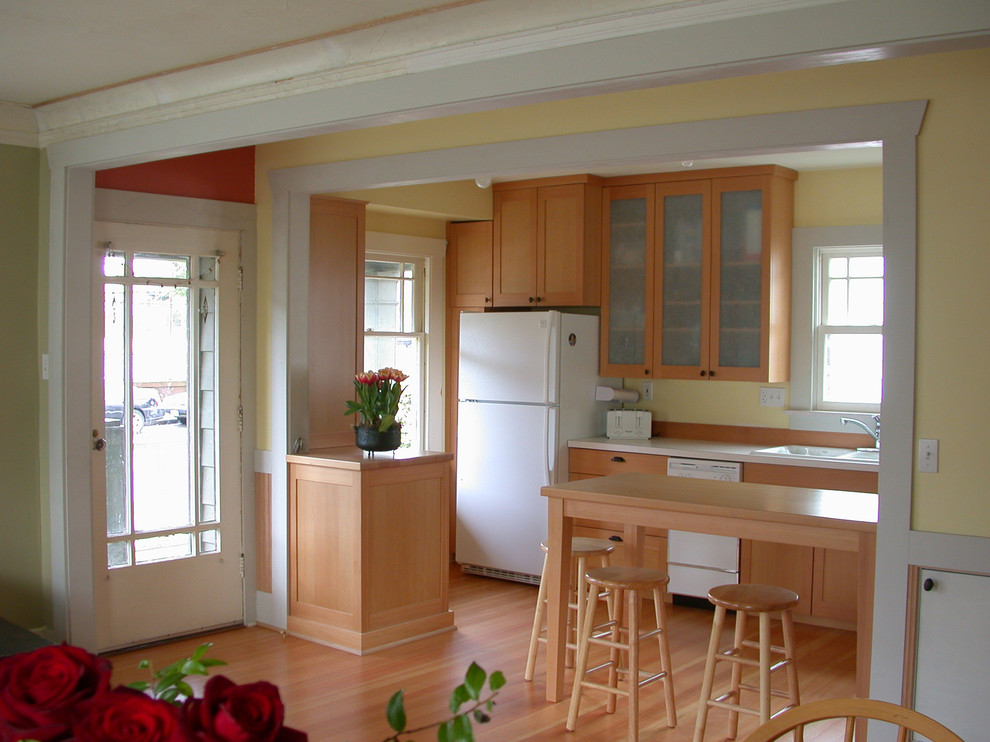 Inredning av ett amerikanskt litet kök, med en nedsänkt diskho, luckor med infälld panel, skåp i mellenmörkt trä, laminatbänkskiva, vita vitvaror, mellanmörkt trägolv och en halv köksö