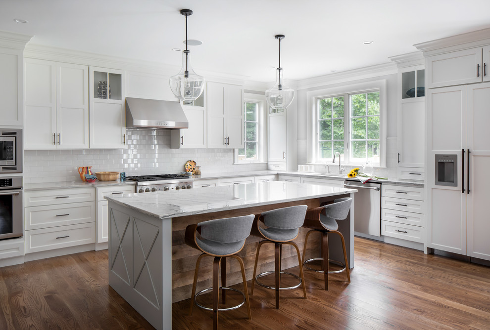 Klassische Küche in L-Form mit Schrankfronten im Shaker-Stil, weißen Schränken, Küchenrückwand in Weiß, Rückwand aus Metrofliesen, Elektrogeräten mit Frontblende, braunem Holzboden, Kücheninsel und grauer Arbeitsplatte in Boston