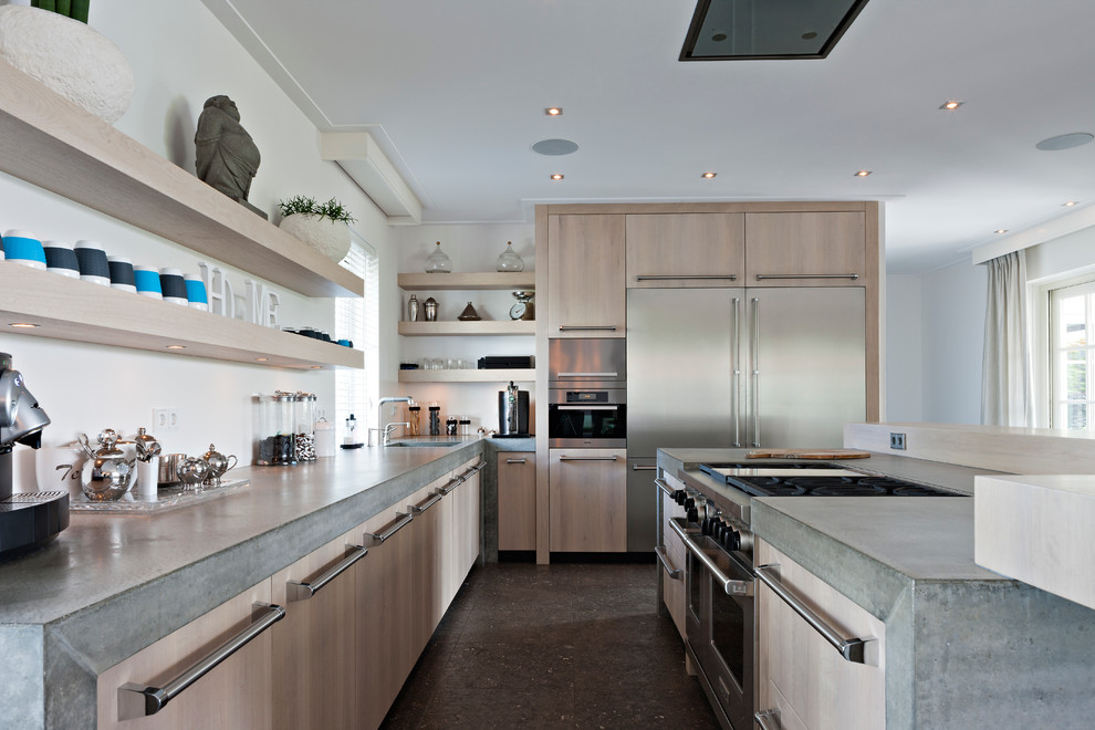 Diseño de cocina contemporánea con armarios con paneles lisos, encimera de cemento, puertas de armario de madera clara y electrodomésticos de acero inoxidable