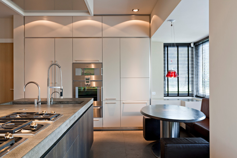 Ejemplo de cocina contemporánea con armarios con paneles lisos, encimera de cemento, electrodomésticos de acero inoxidable y puertas de armario blancas