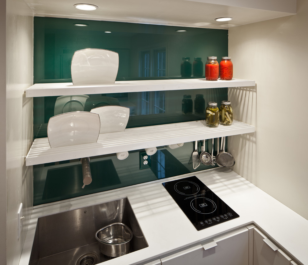 Bild på ett funkis kök, med en undermonterad diskho, släta luckor, vita skåp, bänkskiva i koppar, grönt stänkskydd, glaspanel som stänkskydd och rostfria vitvaror