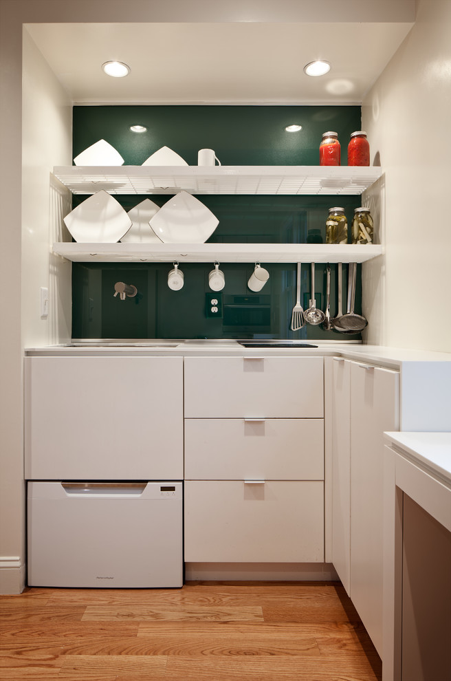 Eat-in kitchen - contemporary u-shaped eat-in kitchen idea in Boston with an undermount sink, flat-panel cabinets, white cabinets, solid surface countertops, green backsplash, glass sheet backsplash and stainless steel appliances