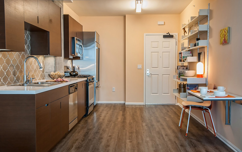 Ejemplo de cocina lineal actual cerrada con armarios con paneles lisos, puertas de armario de madera en tonos medios, fregadero encastrado y electrodomésticos de acero inoxidable