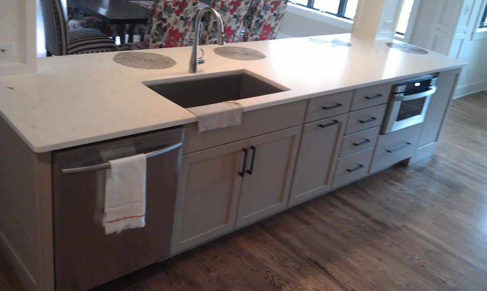 This is an example of a medium sized eclectic galley kitchen/diner in Milwaukee with a single-bowl sink, engineered stone countertops, beige splashback, porcelain splashback, stainless steel appliances, medium hardwood flooring and an island.