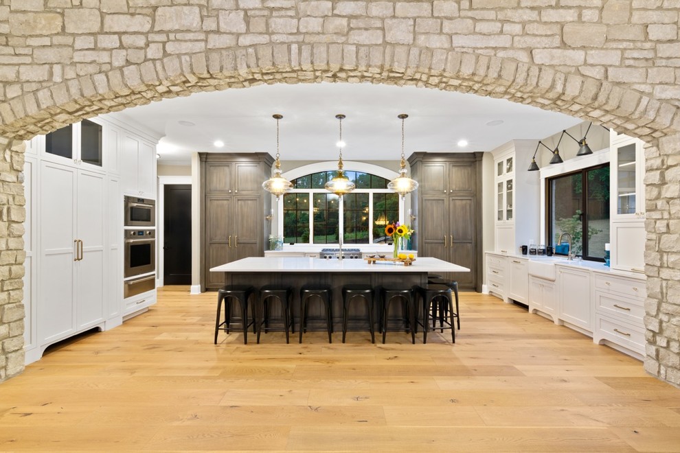 Foto de cocina tradicional renovada grande con fregadero sobremueble, armarios tipo vitrina, puertas de armario de madera oscura, encimera de cuarzo compacto, electrodomésticos con paneles, suelo de madera clara, una isla y encimeras blancas