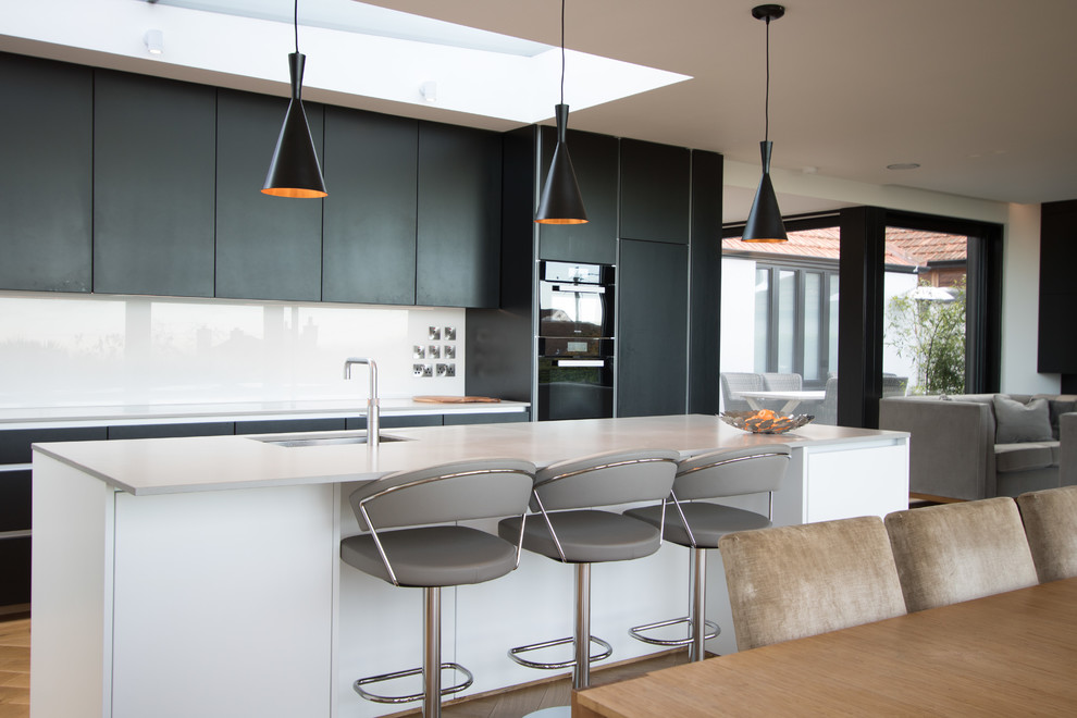 Стильный дизайн: кухня-гостиная в скандинавском стиле с врезной мойкой, плоскими фасадами, белым фартуком, фартуком из стекла, черной техникой, островом и черно-белыми фасадами - последний тренд