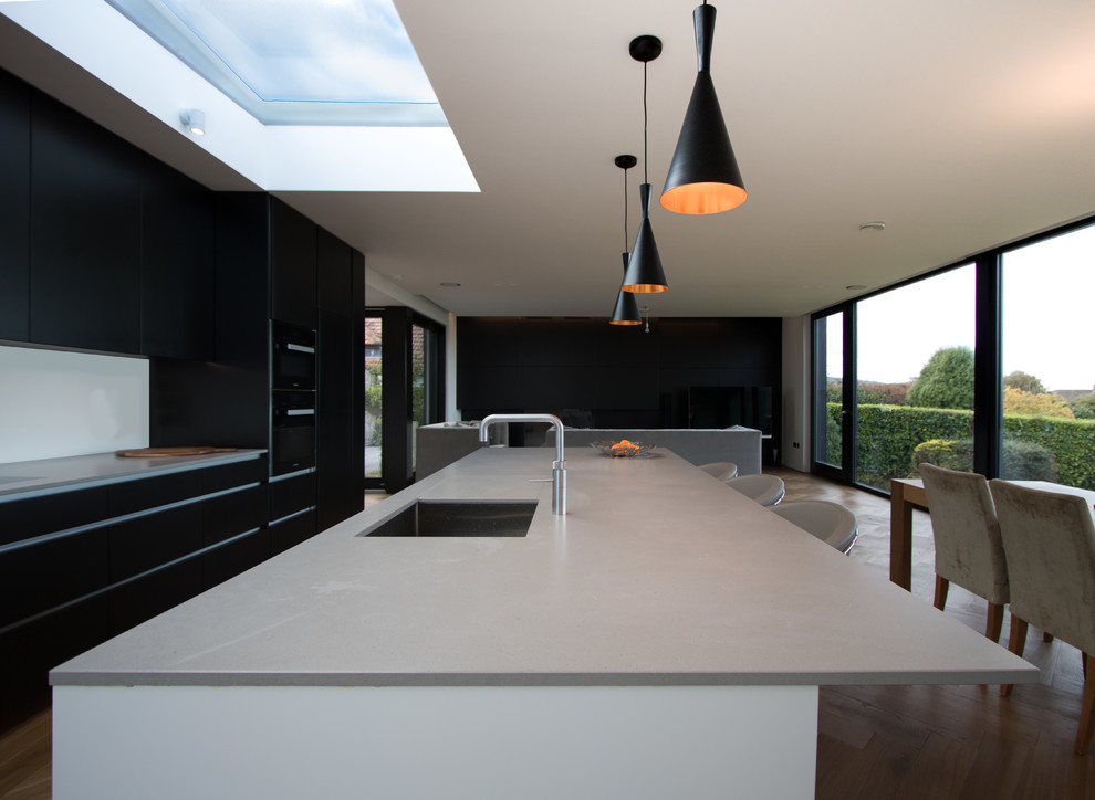 Zweizeilige Moderne Wohnküche mit Unterbauwaschbecken, flächenbündigen Schrankfronten, Küchenrückwand in Weiß, braunem Holzboden und Kücheninsel in Dublin
