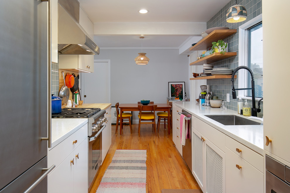 Example of a mid-sized transitional galley medium tone wood floor and beige floor enclosed kitchen design in Los Angeles with an undermount sink, flat-panel cabinets, white cabinets, solid surface countertops, green backsplash, porcelain backsplash, stainless steel appliances, no island and white countertops