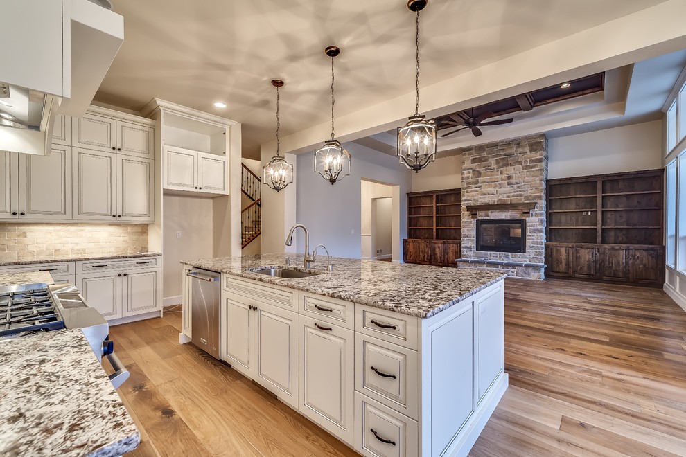 Photo of a large traditional open plan kitchen in Boise with a single-bowl sink, raised-panel cabinets, white cabinets, granite worktops, beige splashback, metro tiled splashback, stainless steel appliances, medium hardwood flooring and an island.