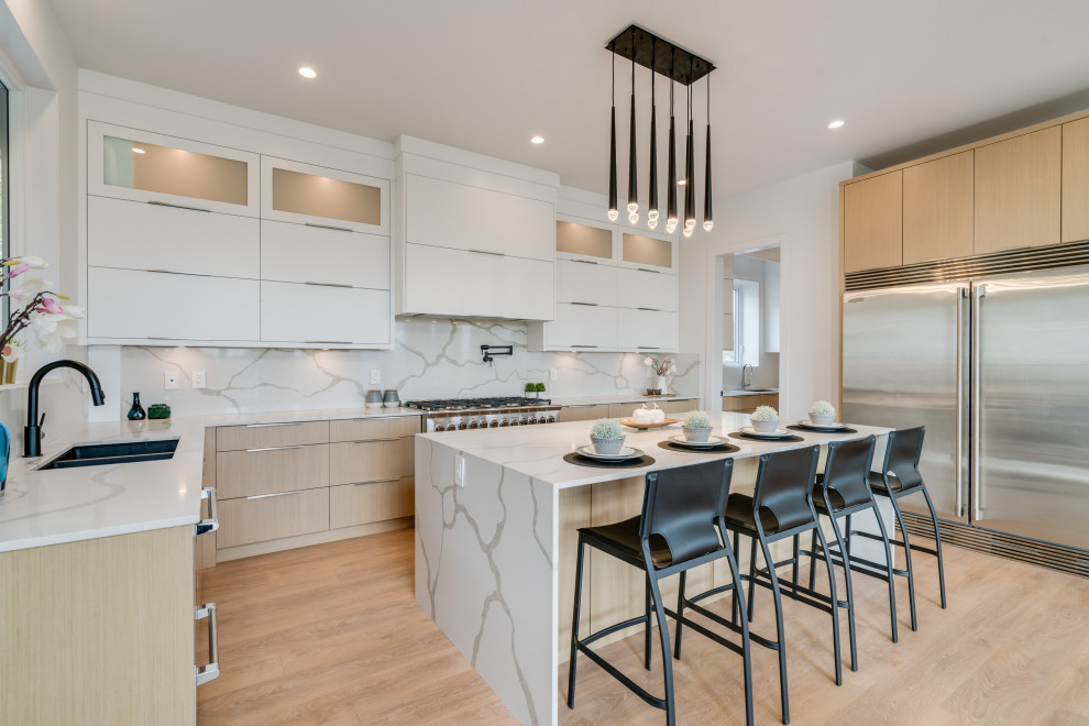 Large contemporary u-shaped kitchen/diner in Vancouver with a submerged sink, flat-panel cabinets, light wood cabinets, engineered stone countertops, grey splashback, engineered quartz splashback, stainless steel appliances, laminate floors, an island, beige floors and white worktops.
