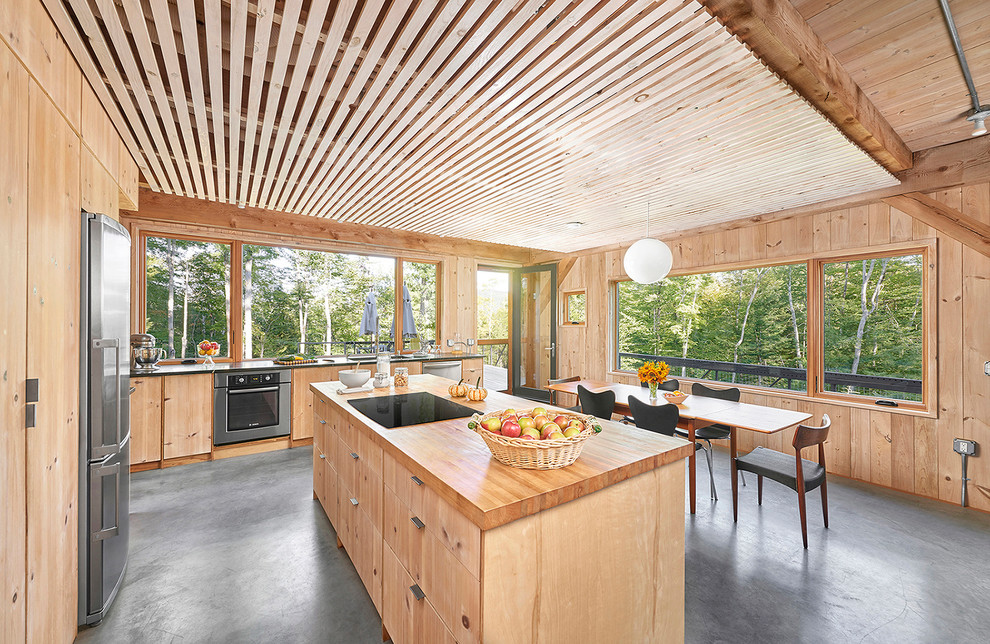 Exemple d'une cuisine américaine montagne en L et bois clair avec un placard à porte plane, un plan de travail en bois, fenêtre, un électroménager en acier inoxydable, îlot et un sol gris.