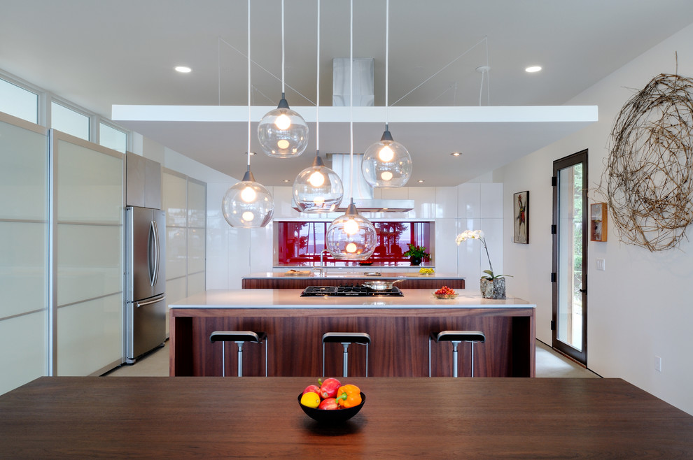 Inspiration for a mid-sized contemporary galley concrete floor eat-in kitchen remodel in Seattle with a double-bowl sink, flat-panel cabinets, dark wood cabinets, solid surface countertops, white backsplash, stone slab backsplash, stainless steel appliances and an island