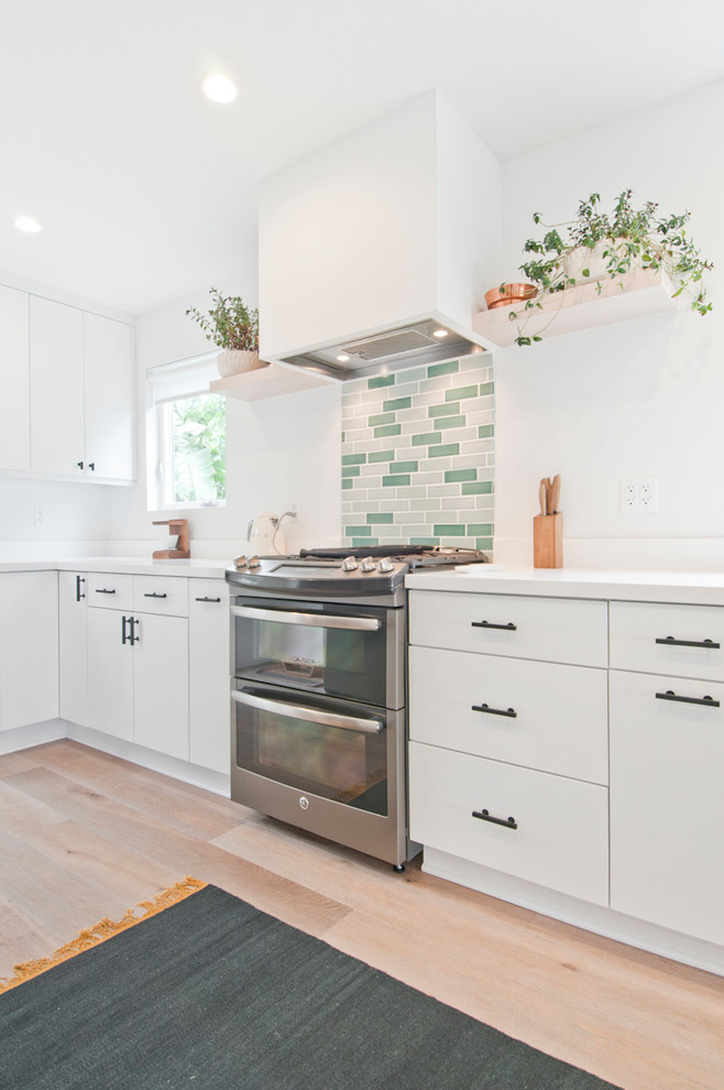 Medium sized retro galley open plan kitchen in Los Angeles with a submerged sink, flat-panel cabinets, white cabinets, engineered stone countertops, green splashback, cement tile splashback, stainless steel appliances, light hardwood flooring, an island and beige floors.