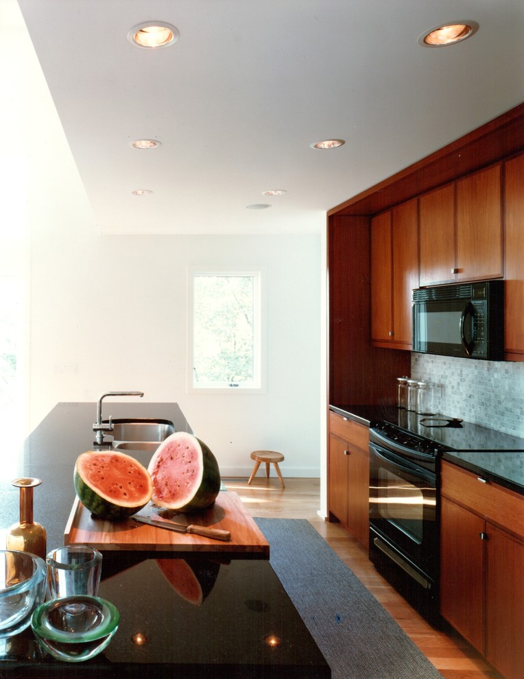 Bild på ett mellanstort funkis l-kök, med släta luckor, stänkskydd i stenkakel, svarta vitvaror, en dubbel diskho, skåp i mellenmörkt trä, vitt stänkskydd och en köksö