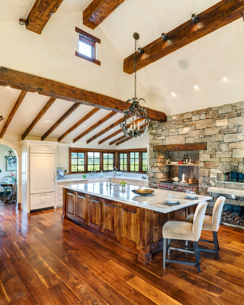 Large mountain style l-shaped medium tone wood floor and brown floor kitchen photo in Other with a farmhouse sink, raised-panel cabinets, white cabinets, quartzite countertops, paneled appliances and an island
