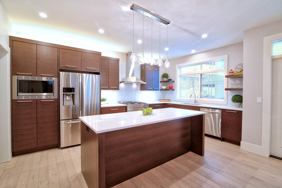 Open concept kitchen - large modern l-shaped light wood floor open concept kitchen idea in Vancouver with an undermount sink, flat-panel cabinets, dark wood cabinets, quartz countertops, white backsplash, glass tile backsplash, stainless steel appliances and an island