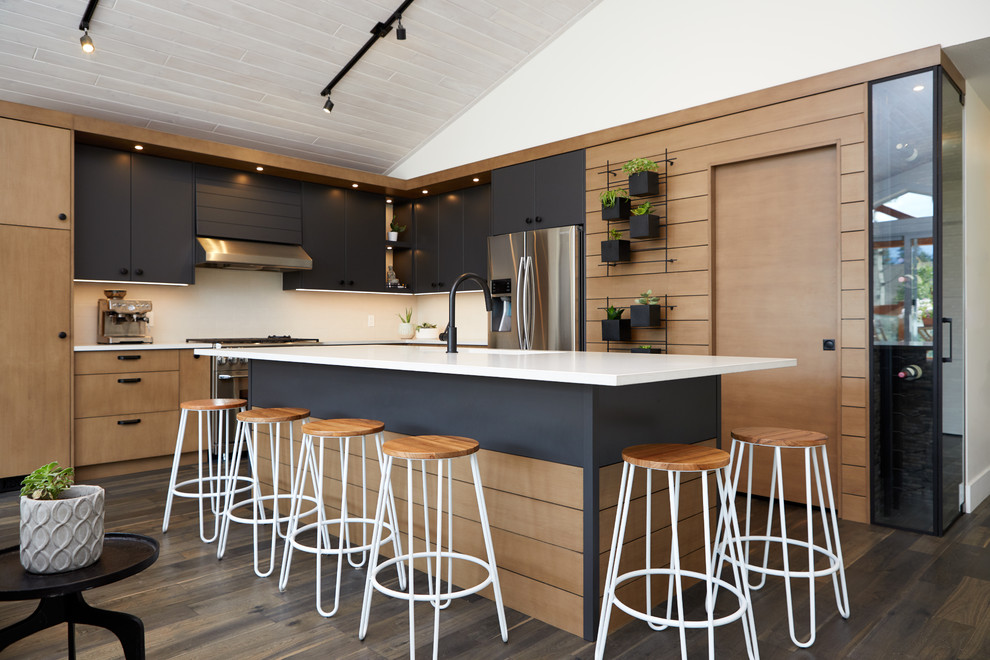 Offene Moderne Küche mit Unterbauwaschbecken, flächenbündigen Schrankfronten, schwarzen Schränken, Küchenrückwand in Weiß, Küchengeräten aus Edelstahl, braunem Holzboden, Kücheninsel, braunem Boden und weißer Arbeitsplatte in Calgary