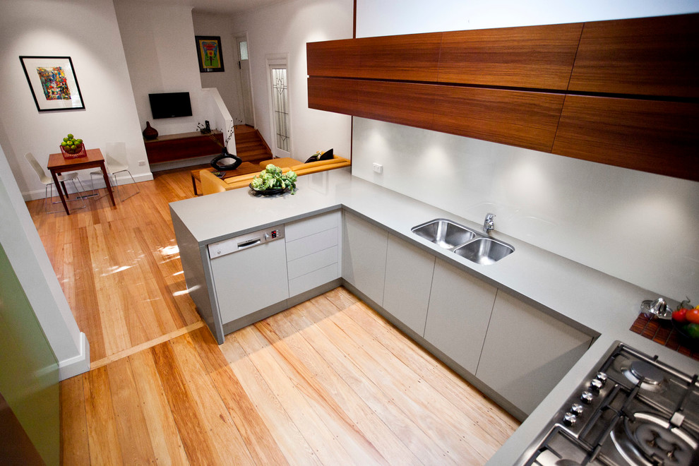 Mid-sized trendy u-shaped light wood floor eat-in kitchen photo in Melbourne with a double-bowl sink, flat-panel cabinets, white cabinets, quartz countertops, white backsplash, glass sheet backsplash, stainless steel appliances and a peninsula