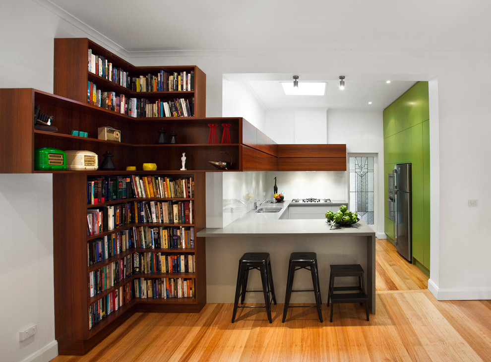 Example of a mid-sized trendy u-shaped light wood floor kitchen design in Melbourne with a peninsula, flat-panel cabinets, green cabinets, quartz countertops, white backsplash, glass sheet backsplash and stainless steel appliances