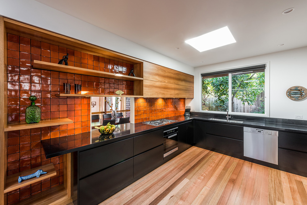 Contemporary l-shaped kitchen in Melbourne with a submerged sink, flat-panel cabinets, black cabinets, engineered stone countertops, orange splashback, cement tile splashback, stainless steel appliances, no island and light hardwood flooring.