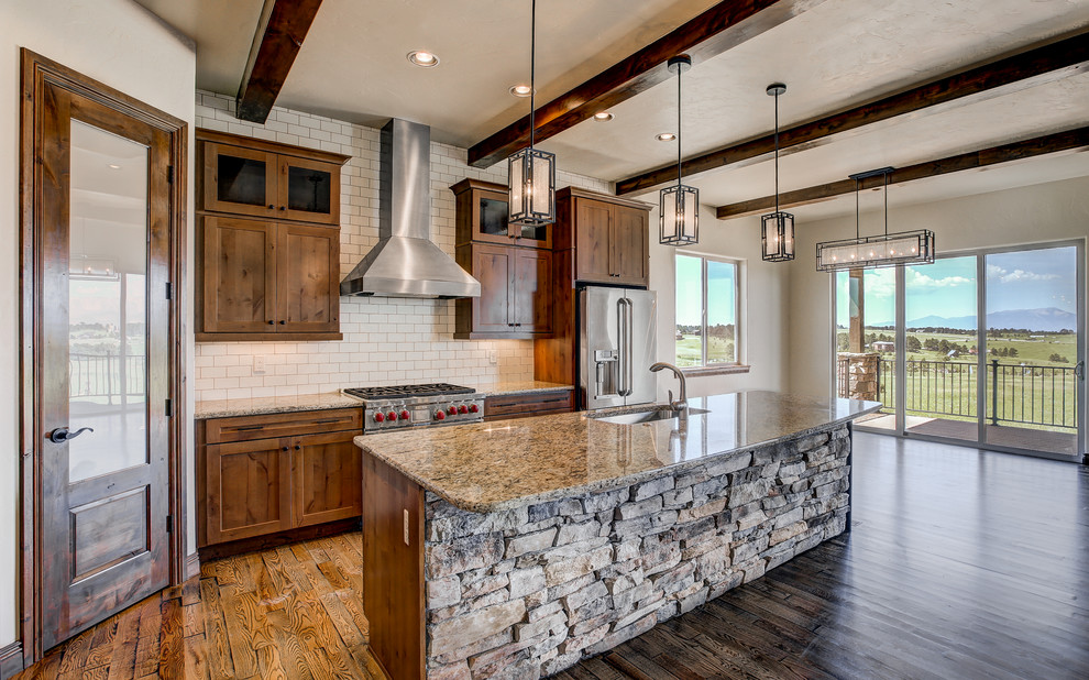 This is an example of a medium sized rustic l-shaped kitchen/diner in Denver with a submerged sink, shaker cabinets, medium wood cabinets, granite worktops, white splashback, metro tiled splashback, stainless steel appliances, medium hardwood flooring and an island.