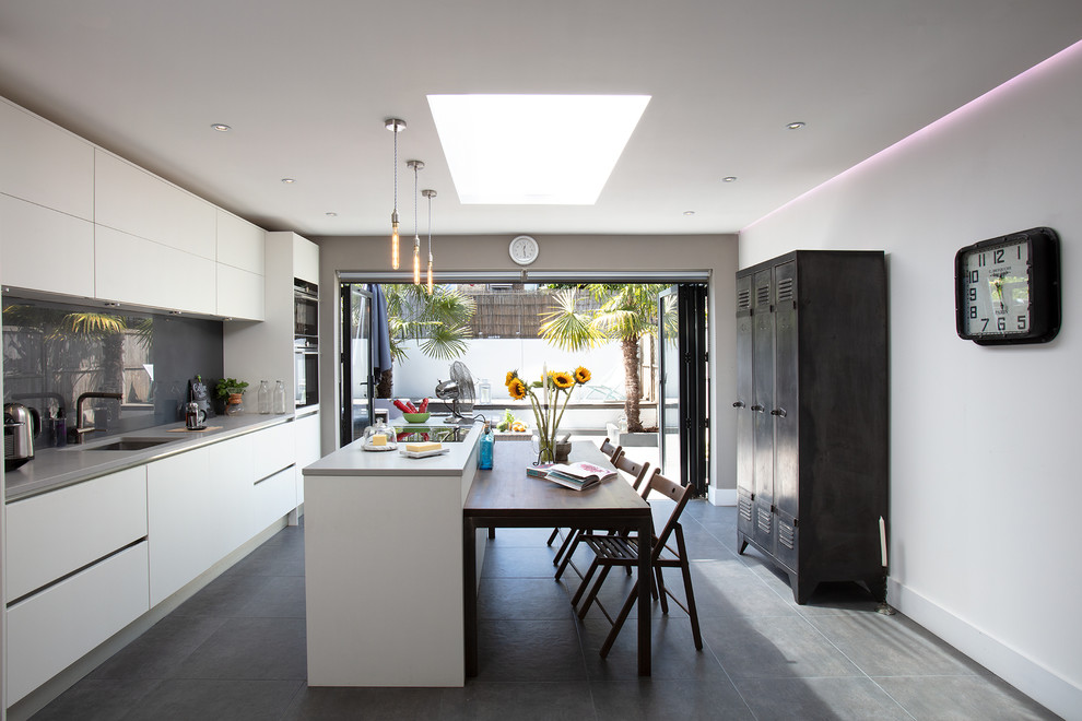 Design ideas for a large contemporary single-wall kitchen in London with an island, a submerged sink, flat-panel cabinets, white cabinets, grey splashback, stainless steel appliances, grey floors, grey worktops and glass sheet splashback.