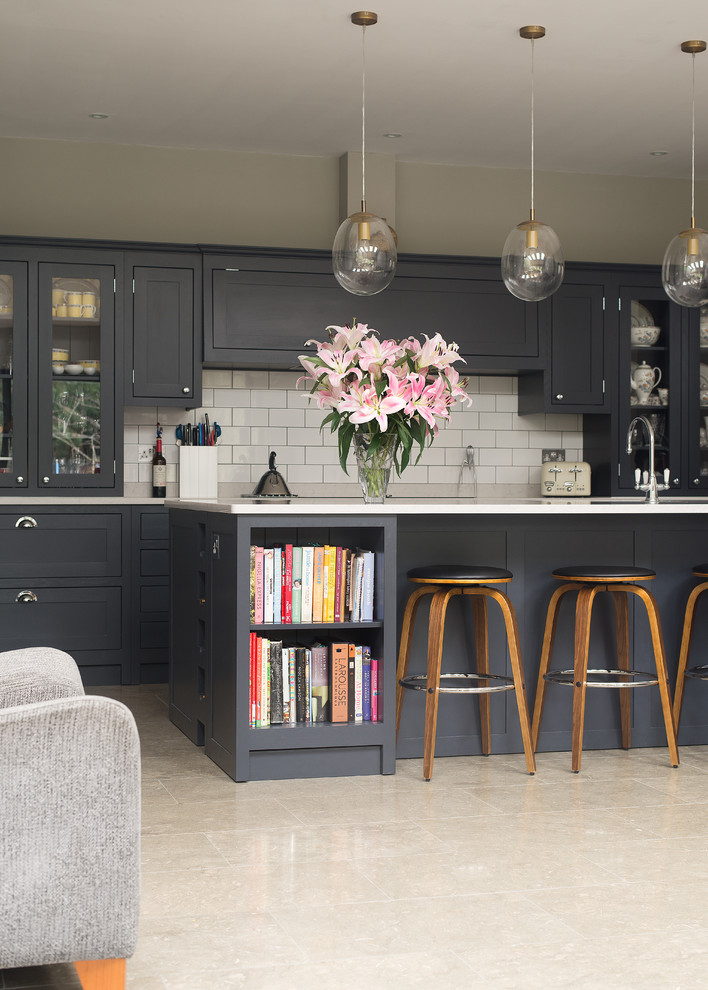 Medium sized classic open plan kitchen in London with a built-in sink, shaker cabinets, dark wood cabinets, marble worktops, white splashback, ceramic splashback, black appliances and an island.