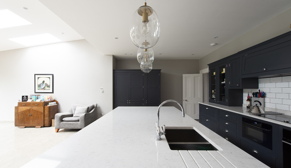 Photo of a traditional open plan kitchen in London with a built-in sink, shaker cabinets, dark wood cabinets, white splashback, ceramic splashback, black appliances and an island.