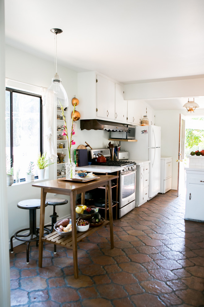 Inspiration for a medium sized bohemian galley enclosed kitchen in Los Angeles with a belfast sink, flat-panel cabinets, white cabinets, quartz worktops, white splashback, metro tiled splashback, stainless steel appliances, terracotta flooring and an island.