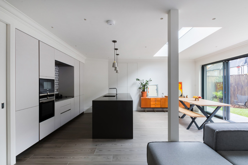 Medium sized contemporary single-wall kitchen/diner in London with a submerged sink, flat-panel cabinets, grey cabinets, multi-coloured splashback, ceramic splashback, stainless steel appliances, light hardwood flooring, an island, grey floors and black worktops.