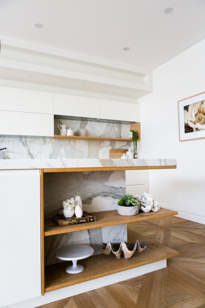 Bild på ett mellanstort funkis kök, med släta luckor, vita skåp, marmorbänkskiva, grått stänkskydd, stänkskydd i marmor, rostfria vitvaror, ljust trägolv och en köksö