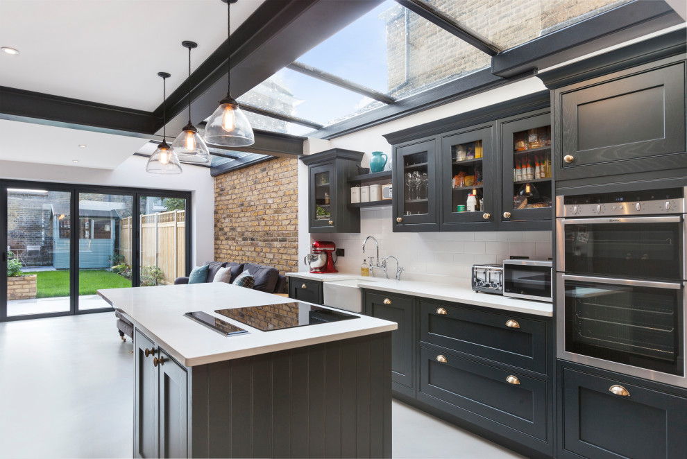 Photo of a contemporary l-shaped open plan kitchen in Other with a belfast sink, shaker cabinets, black cabinets, white splashback, metro tiled splashback, stainless steel appliances, an island, grey floors and white worktops.