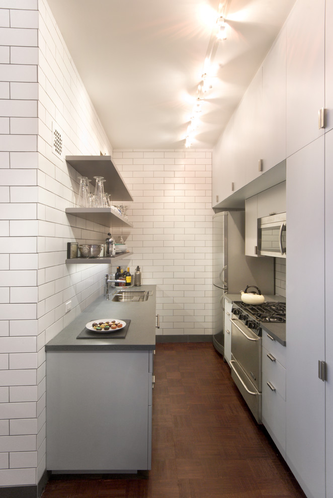 Photo of a contemporary galley enclosed kitchen in New York with a submerged sink, open cabinets, grey cabinets, white splashback, metro tiled splashback and stainless steel appliances.