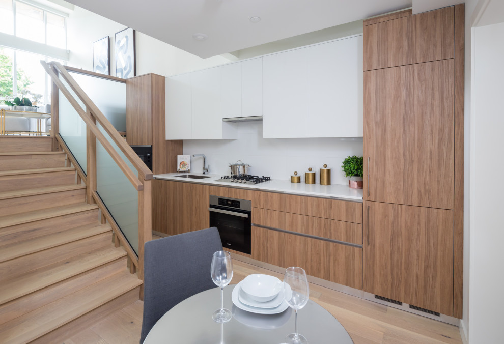 Photo of a contemporary single-wall kitchen/diner in Vancouver with a submerged sink, flat-panel cabinets, medium wood cabinets, white splashback, integrated appliances, medium hardwood flooring, no island and white worktops.