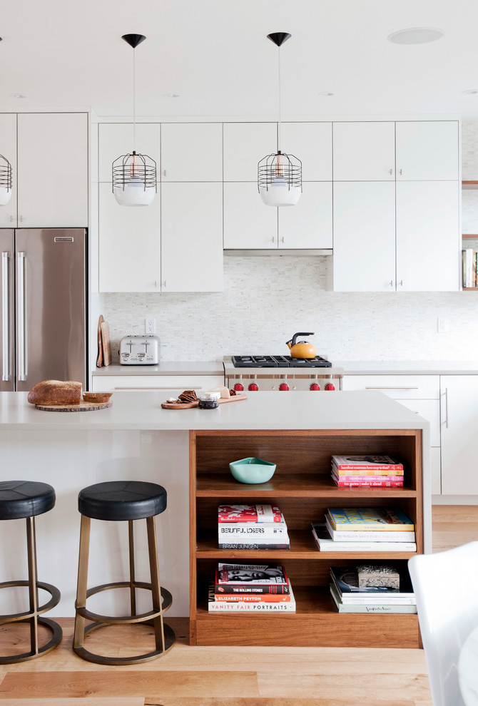Moderne Küche mit flächenbündigen Schrankfronten, weißen Schränken, Küchenrückwand in Weiß, Küchengeräten aus Edelstahl, hellem Holzboden und Kücheninsel in Vancouver