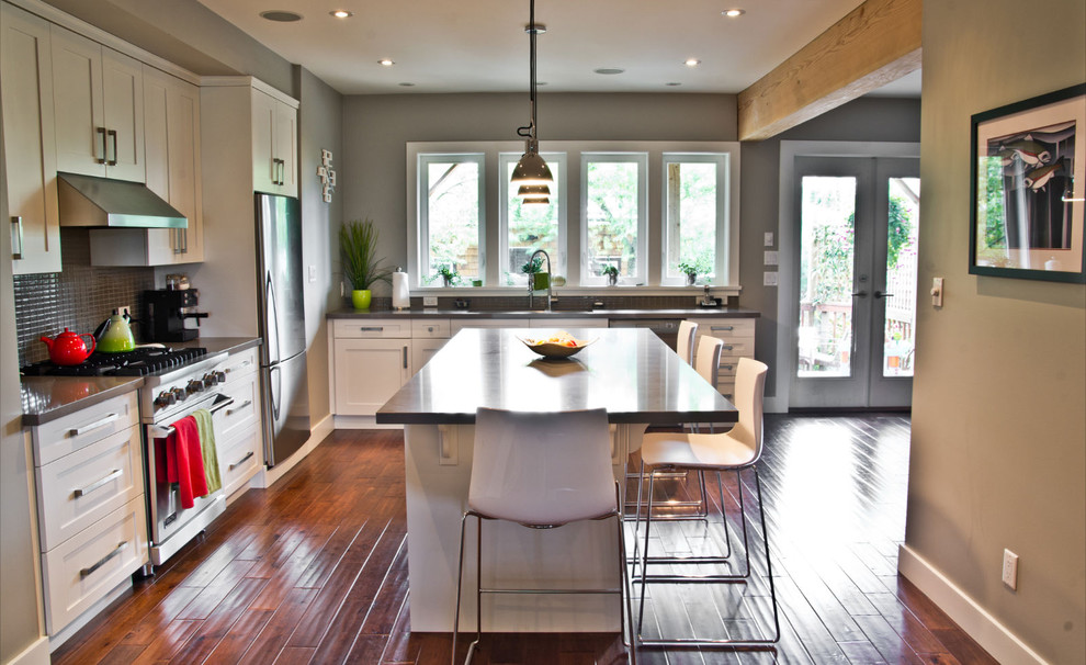 Bild på ett funkis l-kök, med stänkskydd i mosaik, rostfria vitvaror, vita skåp, skåp i shakerstil och stänkskydd med metallisk yta