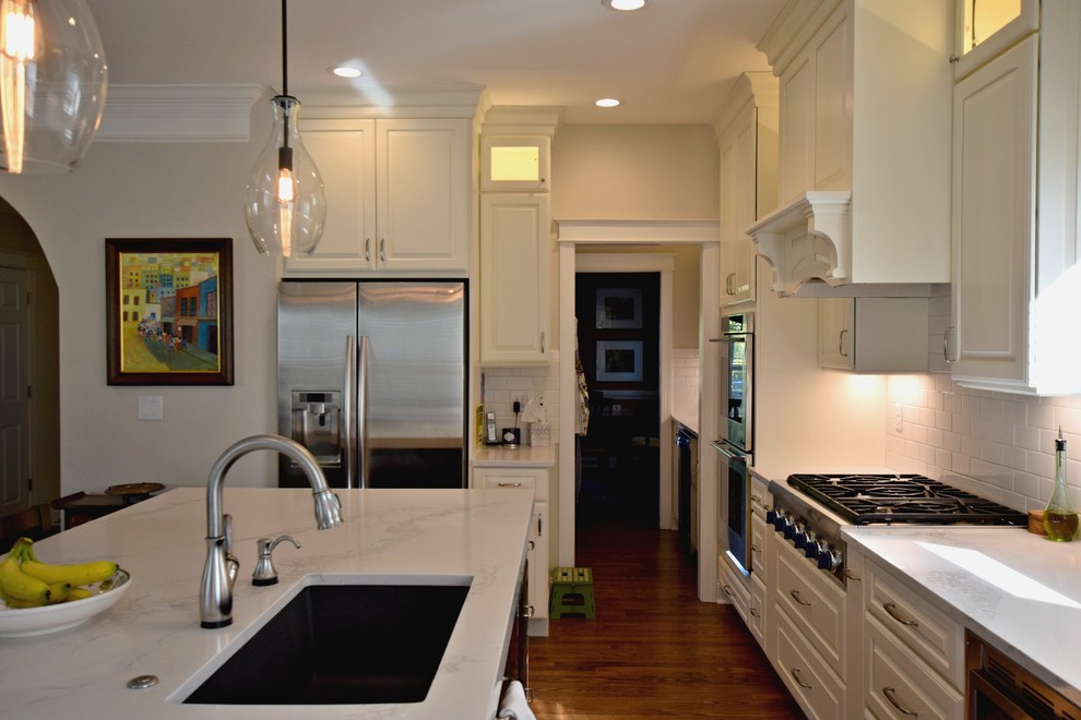 Example of a classic l-shaped medium tone wood floor eat-in kitchen design in Denver with an undermount sink, raised-panel cabinets, white cabinets, quartz countertops, white backsplash, subway tile backsplash, stainless steel appliances and an island