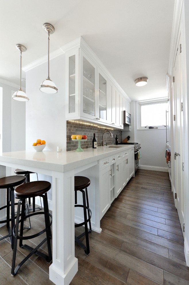 Mid-sized transitional galley medium tone wood floor eat-in kitchen photo in New York with recessed-panel cabinets, white cabinets, solid surface countertops, gray backsplash, stone tile backsplash, stainless steel appliances and an integrated sink