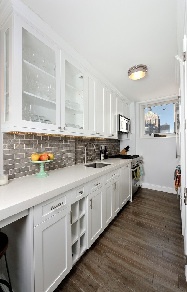 Example of a mid-sized transitional galley medium tone wood floor eat-in kitchen design in New York with an integrated sink, raised-panel cabinets, white cabinets, solid surface countertops, gray backsplash, stone tile backsplash and stainless steel appliances