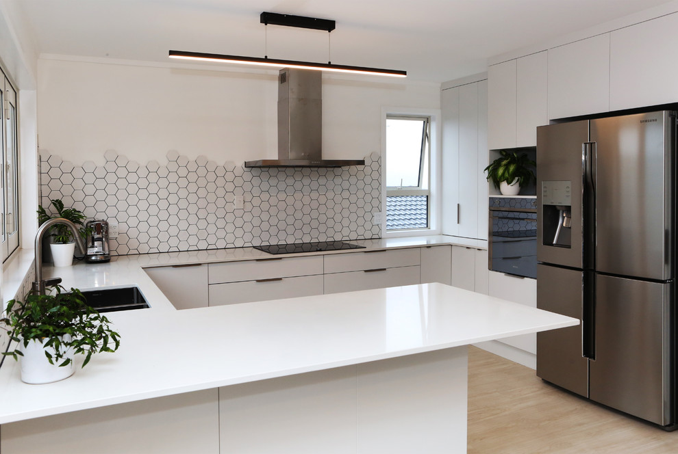 Design ideas for a medium sized modern u-shaped open plan kitchen in Auckland with a submerged sink, flat-panel cabinets, white cabinets, engineered stone countertops, white splashback, mosaic tiled splashback, stainless steel appliances, light hardwood flooring, a breakfast bar and yellow floors.