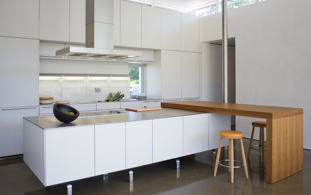 Inspiration för moderna linjära grått kök och matrum, med en undermonterad diskho, släta luckor, vita skåp, bänkskiva i rostfritt stål, vitt stänkskydd, glaspanel som stänkskydd, integrerade vitvaror, betonggolv och en köksö