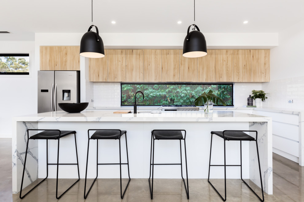 Moderne Küche in L-Form mit Unterbauwaschbecken, flächenbündigen Schrankfronten, weißen Schränken, Küchenrückwand in Weiß, Rückwand-Fenster, Küchengeräten aus Edelstahl, Betonboden, Kücheninsel, grauem Boden und weißer Arbeitsplatte in Melbourne