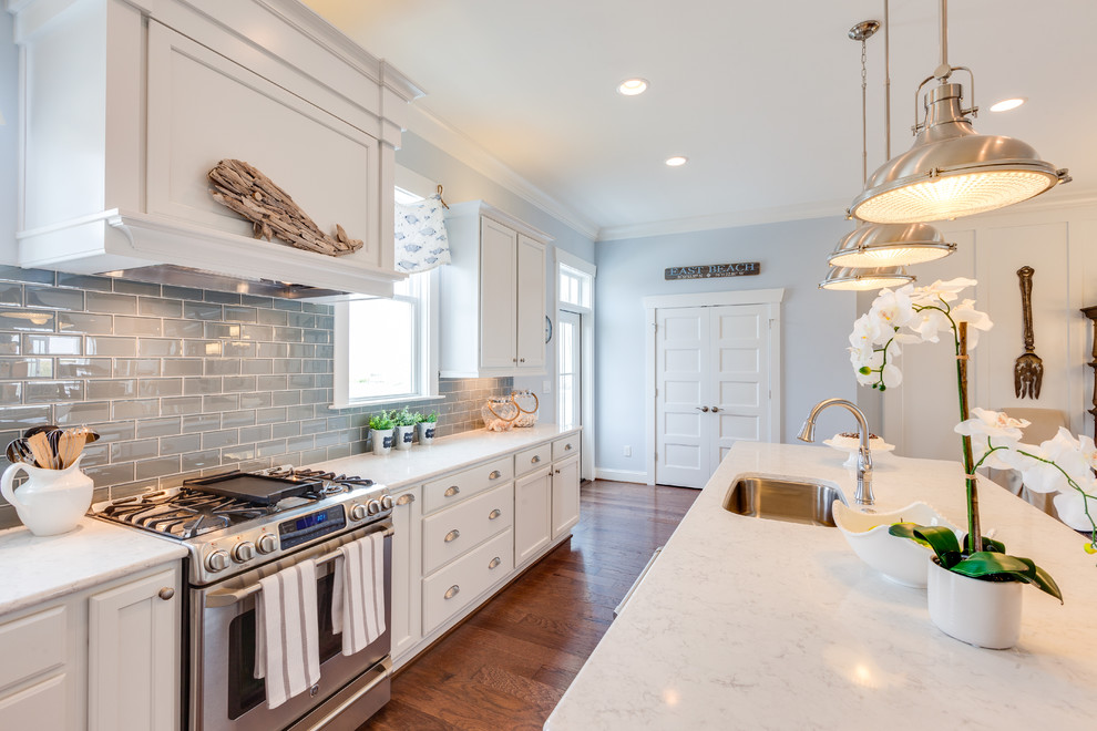 Photo of a large nautical l-shaped open plan kitchen in Other with a submerged sink, shaker cabinets, white cabinets, engineered stone countertops, blue splashback, glass tiled splashback, stainless steel appliances, medium hardwood flooring and an island.