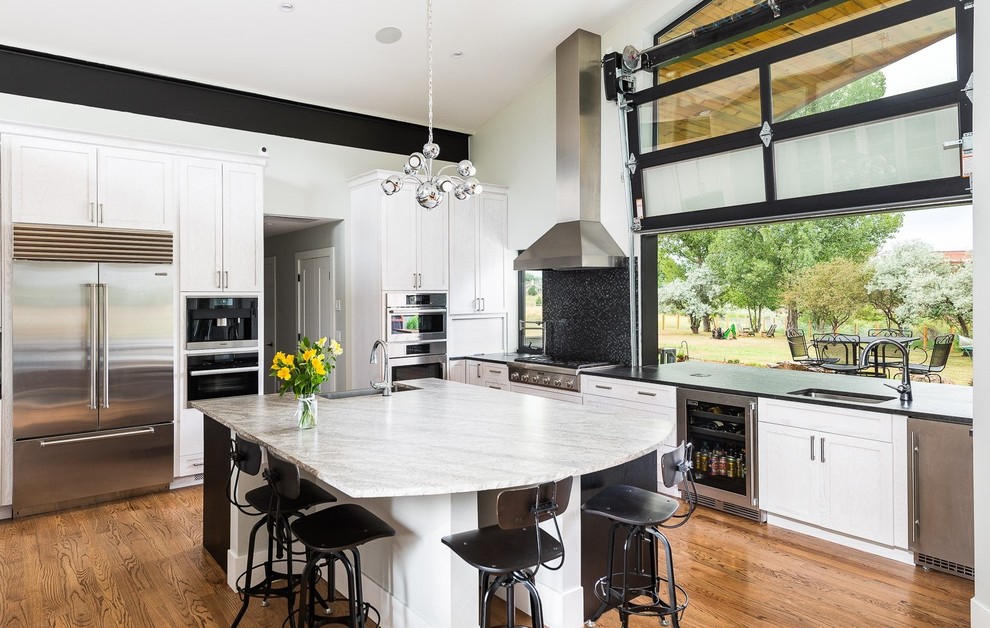 Example of a transitional medium tone wood floor kitchen design in Denver with an undermount sink, shaker cabinets, stainless steel appliances, an island and black countertops