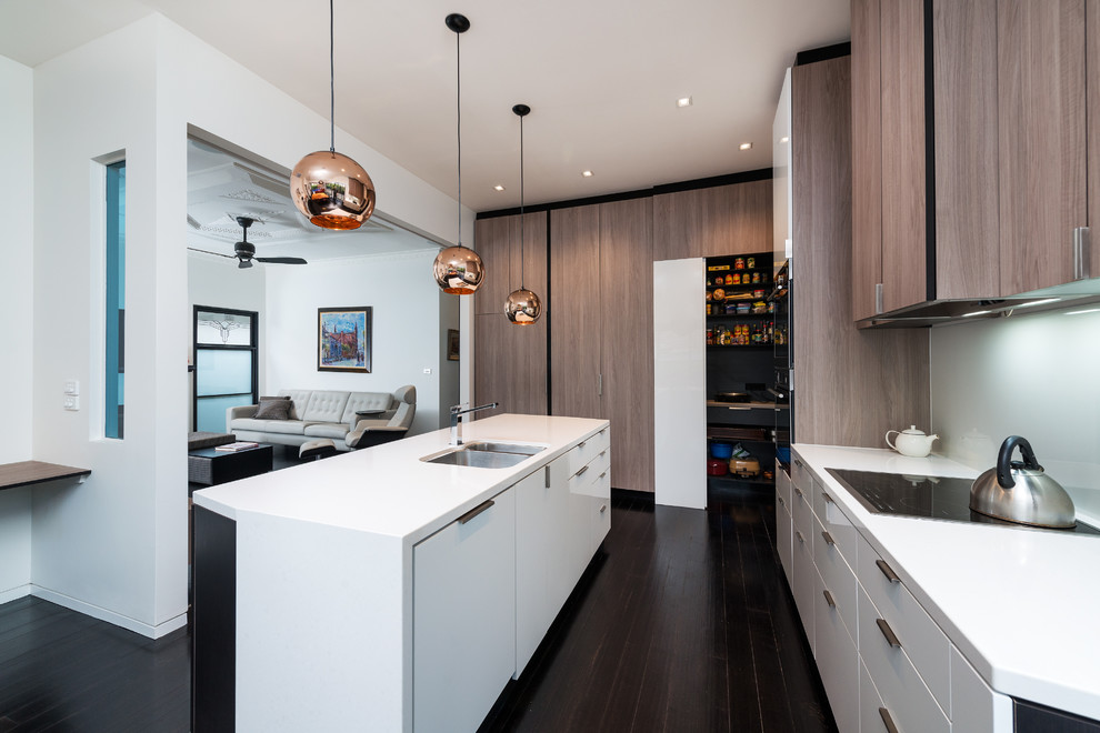 Cette photo montre une cuisine tendance en L et bois brun avec un placard à porte plane, une crédence grise, une crédence en feuille de verre, parquet foncé et îlot.