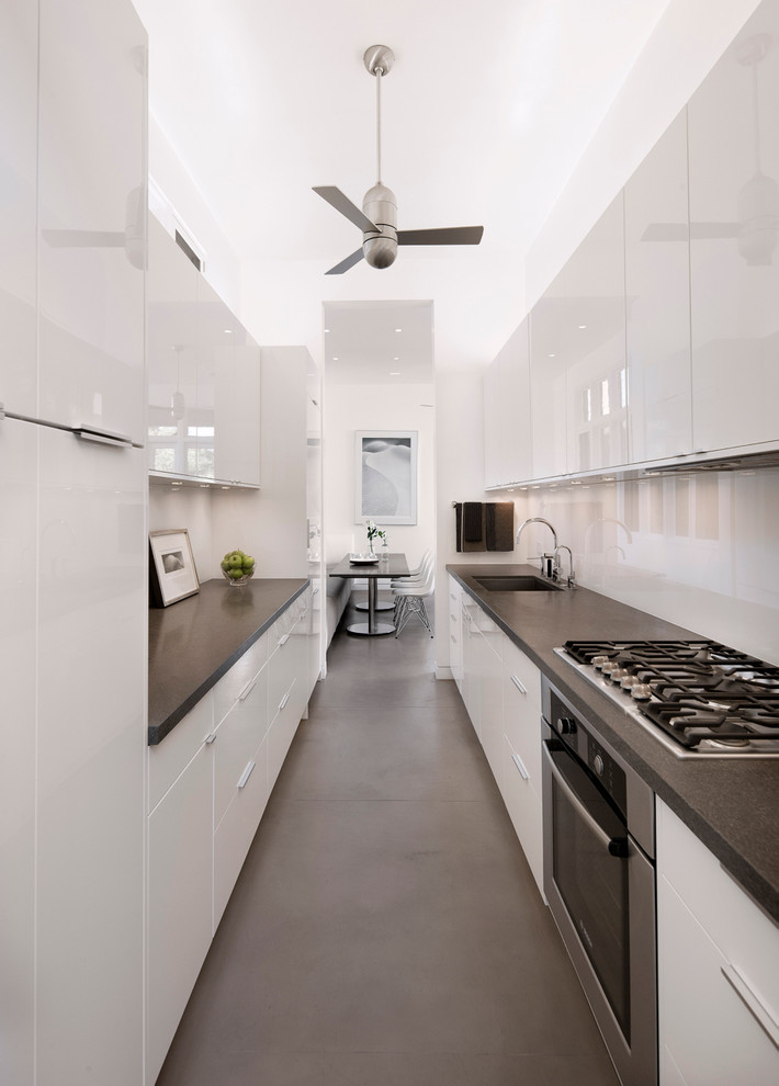 Zweizeilige Moderne Küche in grau-weiß ohne Insel mit weißen Schränken, Küchengeräten aus Edelstahl, Waschbecken, flächenbündigen Schrankfronten, Küchenrückwand in Weiß, Glasrückwand und Betonboden in Santa Barbara