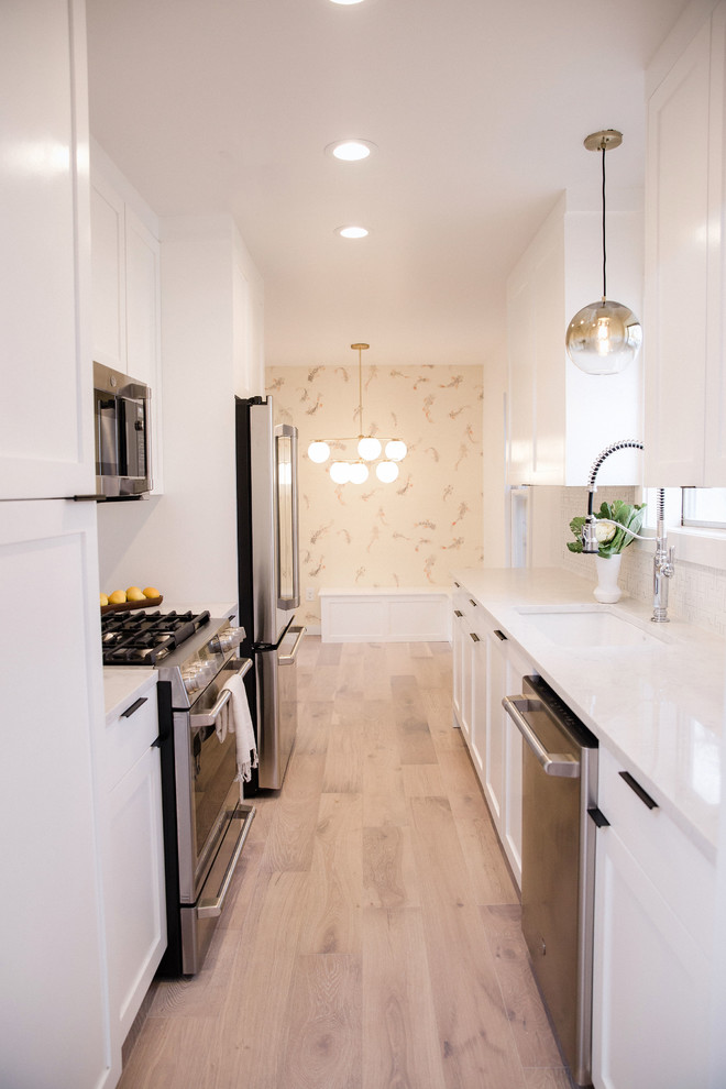 Foto på ett litet funkis vit kök, med en dubbel diskho, skåp i shakerstil, bänkskiva i kvartsit, vitt stänkskydd, rostfria vitvaror, brunt golv, vita skåp och ljust trägolv