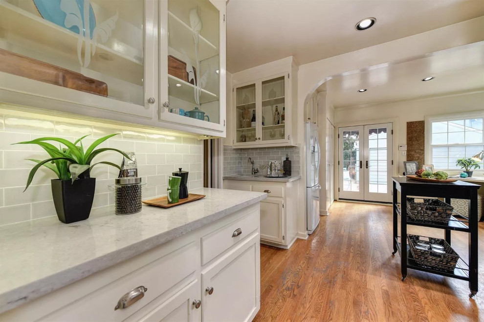 Mid-sized elegant galley medium tone wood floor and multicolored floor enclosed kitchen photo in Sacramento with a farmhouse sink, glass-front cabinets, quartzite countertops, gray backsplash, subway tile backsplash, stainless steel appliances, no island and gray countertops