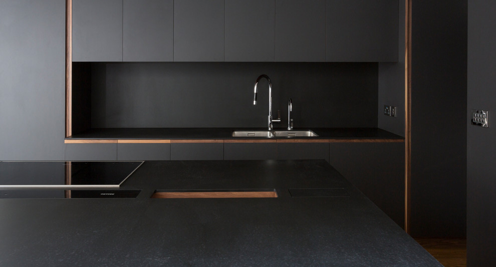Medium sized contemporary single-wall kitchen/diner in London with a double-bowl sink, flat-panel cabinets, black cabinets, black splashback, medium hardwood flooring, an island and brown floors.